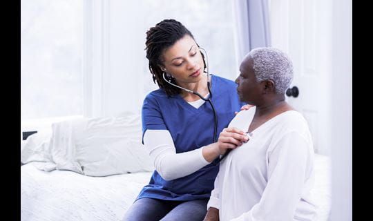 Black female nurse uses stethoscope on older Black female patient